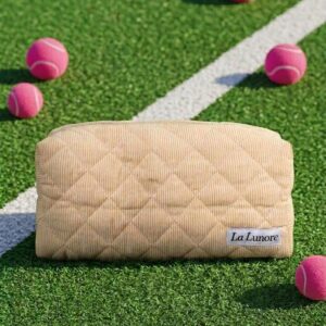 Crèmekleurige gewatteerde La Lunore toilettas met merklogo op groen kunstgras met roze tennisballen.
