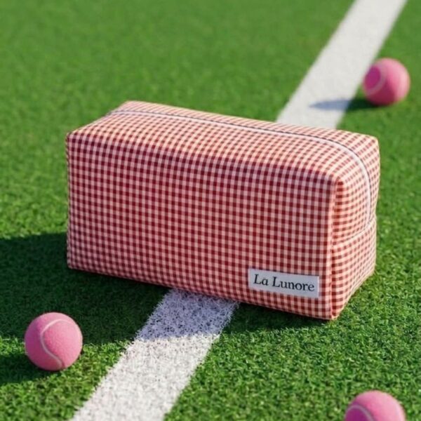 Rood-wit geruite La Lunore toilettas met wit merklogo op groen kunstgras met roze tennisballen.