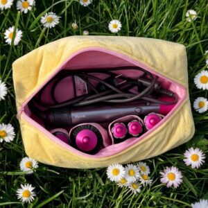 Gele en roze La Lunore Sunshine toilettas met velvet afwerking, gesloten met roze rits, op zand met citroen en handdoek.
